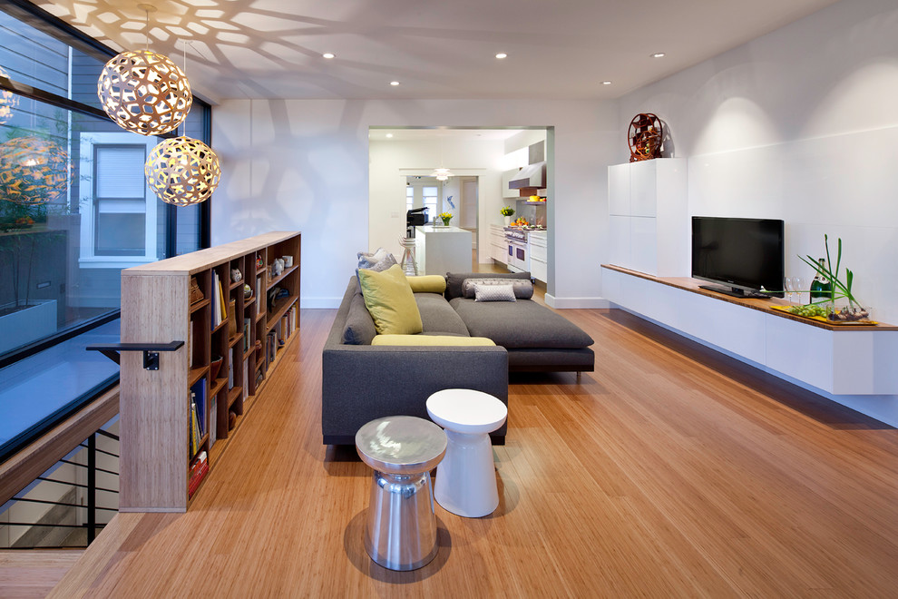 Modelo de salón abierto moderno sin chimenea con paredes blancas, suelo de madera en tonos medios y televisor independiente