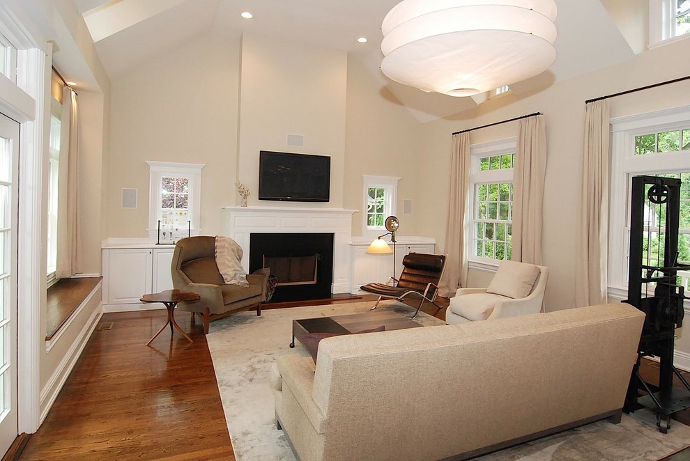 Idee per un soggiorno minimal con pareti beige, pavimento in legno massello medio, camino classico e TV a parete