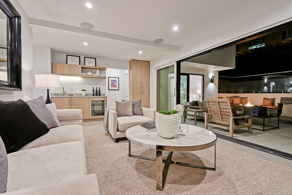 Modelo de sala de estar con barra de bar abierta de tamaño medio con paredes blancas, suelo de baldosas de porcelana, televisor colgado en la pared y suelo gris