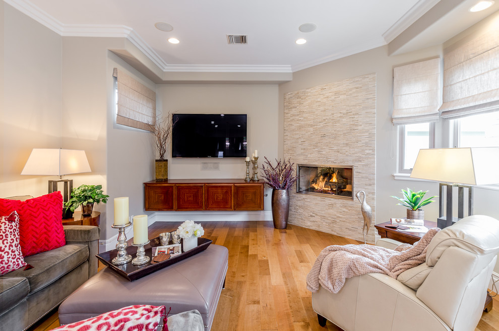 Inspiration for a medium sized traditional open plan games room in Los Angeles with a wall mounted tv, beige walls, medium hardwood flooring, a hanging fireplace, a tiled fireplace surround and brown floors.