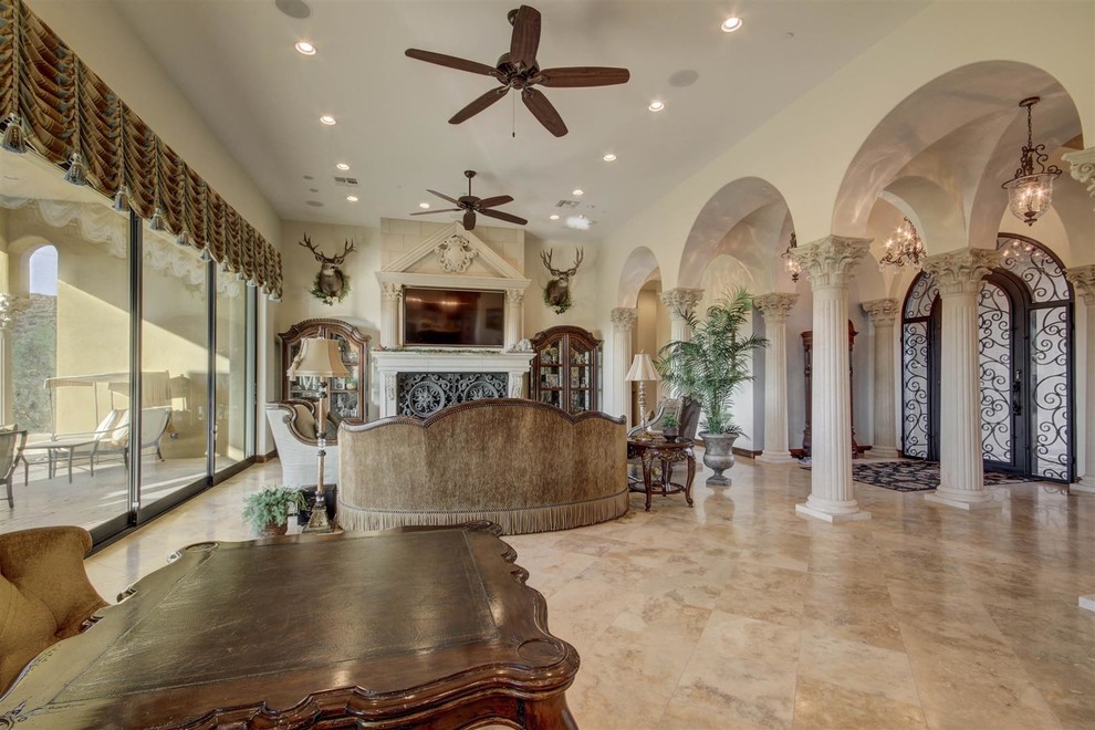 This is an example of a large mediterranean open plan games room in Phoenix with beige walls, travertine flooring, a standard fireplace, a plastered fireplace surround, a wall mounted tv and beige floors.