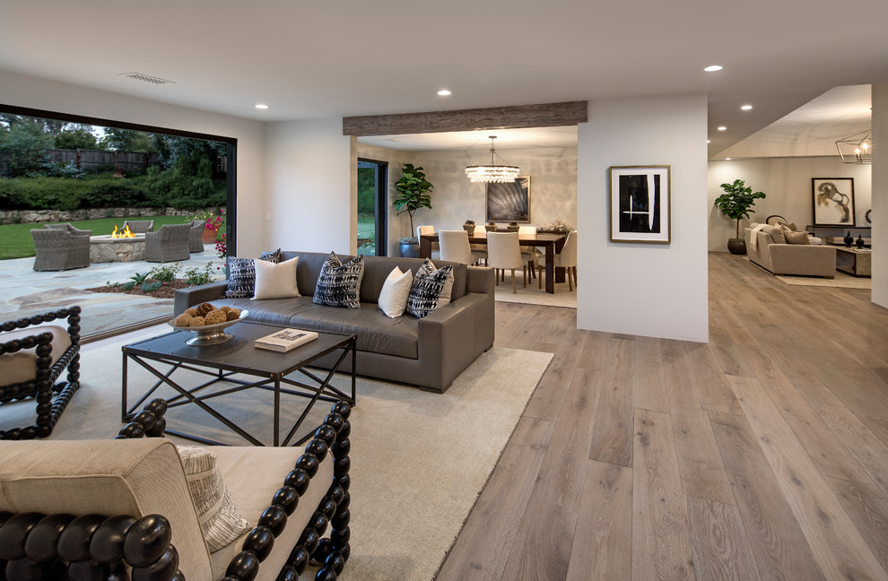 Modelo de sala de estar abierta contemporánea grande sin chimenea y televisor con paredes blancas, suelo de madera clara y suelo gris