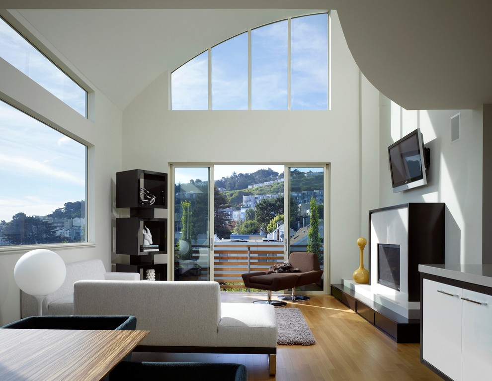 Пример оригинального дизайна: открытая гостиная комната в современном стиле с белыми стенами, паркетным полом среднего тона, стандартным камином и телевизором на стене