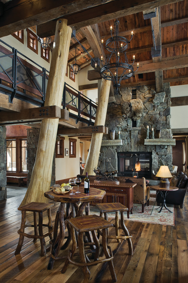 Inspiration pour une salle à manger chalet avec un mur beige, parquet foncé, une cheminée double-face et un manteau de cheminée en pierre.