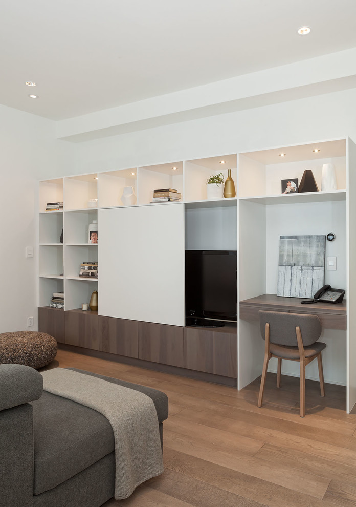 Cette image montre une grande salle de séjour design avec un mur blanc, un sol en bois brun et un téléviseur dissimulé.