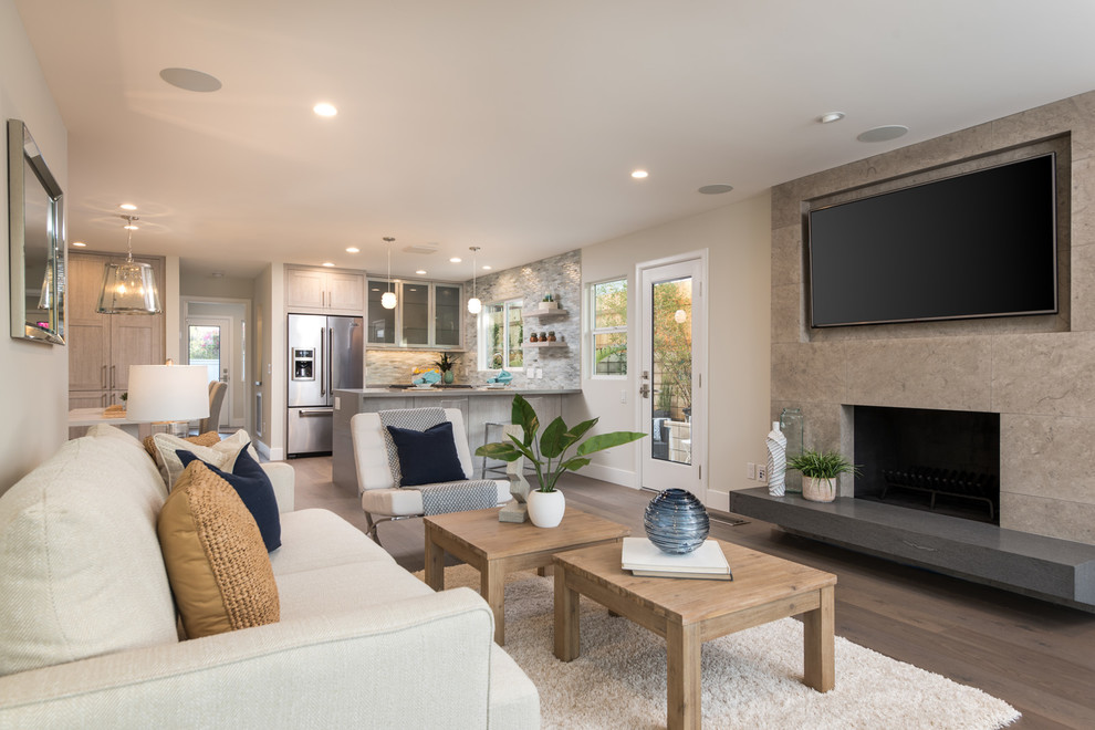 Mittelgroßes, Offenes Modernes Wohnzimmer mit grauer Wandfarbe, braunem Holzboden, Kamin, Kaminumrandung aus Stein, TV-Wand und grauem Boden in San Diego