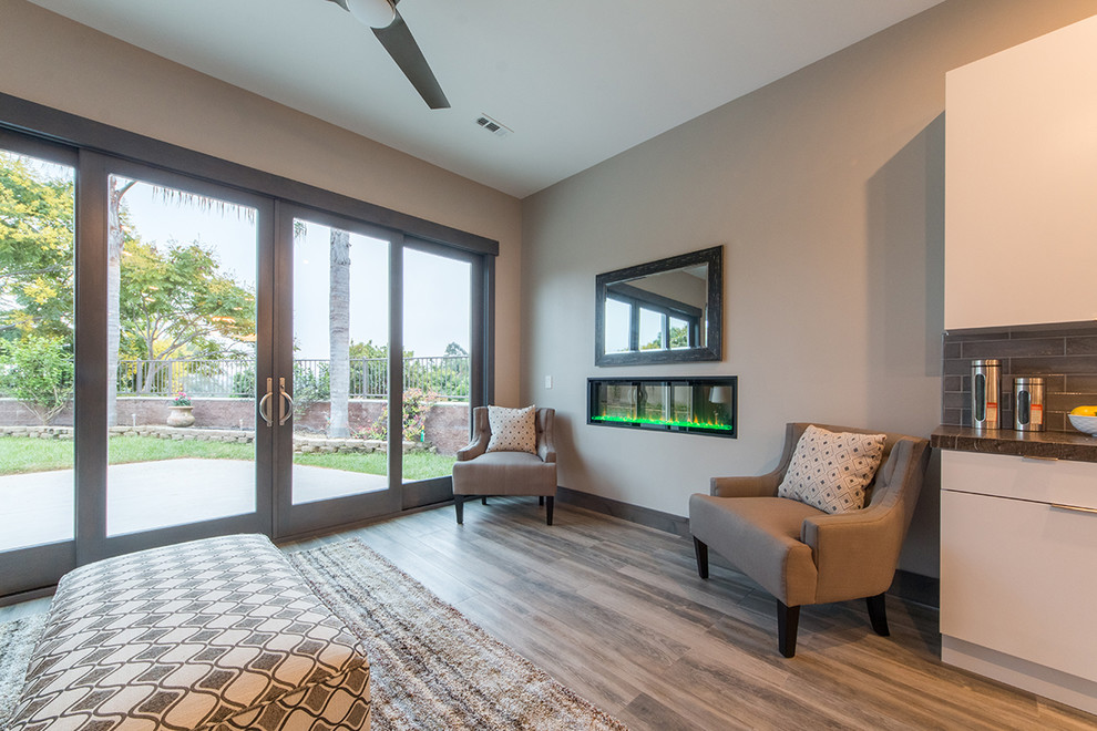 Foto de sala de estar abierta contemporánea pequeña sin televisor con paredes grises, suelo laminado, chimenea lineal, marco de chimenea de metal y suelo marrón