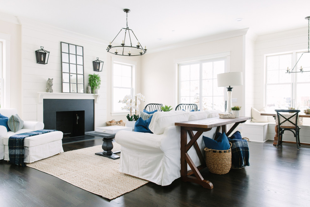 Imagen de sala de estar abierta de estilo de casa de campo de tamaño medio con paredes beige, suelo de madera oscura, todas las chimeneas y marco de chimenea de piedra
