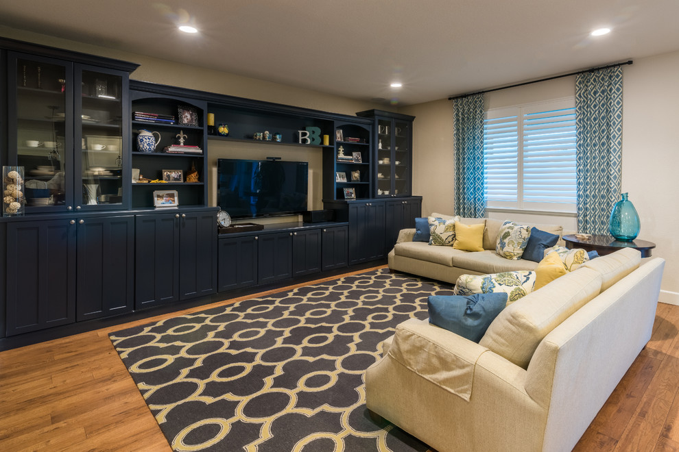Modelo de sala de estar abierta actual grande sin chimenea con paredes beige, suelo de madera clara y televisor colgado en la pared