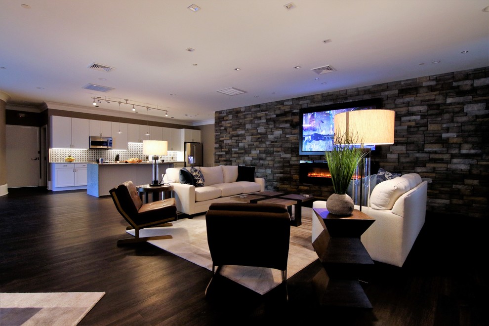 На фото: большая открытая гостиная комната в стиле модернизм с бежевыми стенами, полом из винила, подвесным камином, фасадом камина из камня, скрытым телевизором и коричневым полом