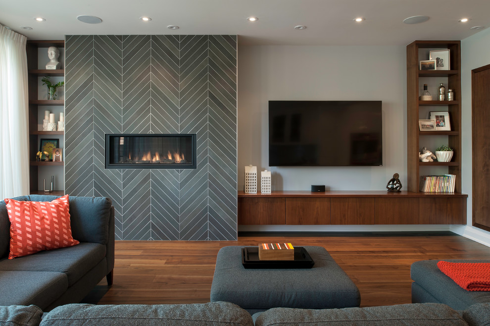 Idée de décoration pour une grande salle de séjour minimaliste ouverte avec un bar de salon, un mur gris, un sol en bois brun, une cheminée ribbon, un sol marron, un manteau de cheminée en carrelage et un téléviseur fixé au mur.