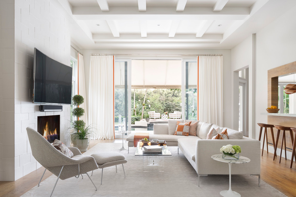 Mittelgroßes, Offenes Modernes Wohnzimmer mit weißer Wandfarbe, braunem Holzboden, Kamin, gefliester Kaminumrandung und TV-Wand in Miami
