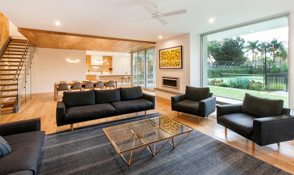 Imagen de sala de estar abierta actual de tamaño medio con paredes blancas, suelo de madera en tonos medios, marco de chimenea de yeso y chimenea lineal