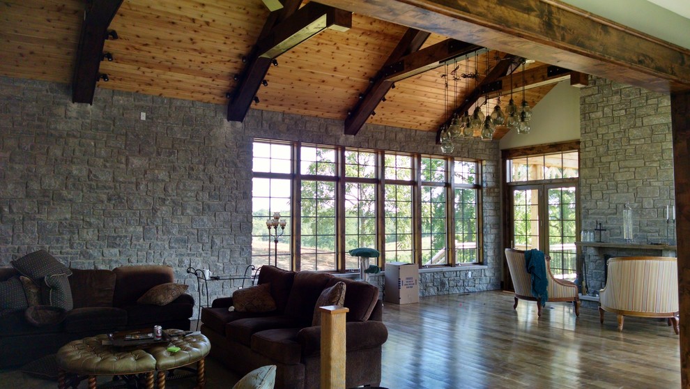 Imagen de sala de estar abierta rústica grande con paredes beige, suelo de madera en tonos medios, todas las chimeneas, marco de chimenea de ladrillo y suelo marrón