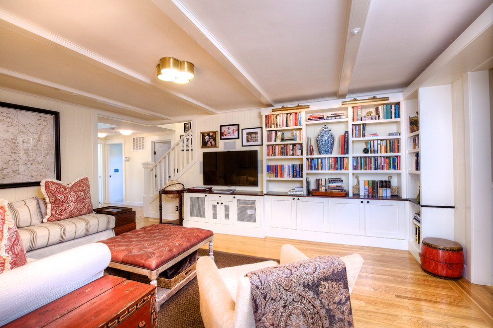 Cette photo montre une salle de séjour craftsman de taille moyenne et ouverte avec une bibliothèque ou un coin lecture, un mur blanc, un sol en bois brun, aucune cheminée et un téléviseur fixé au mur.