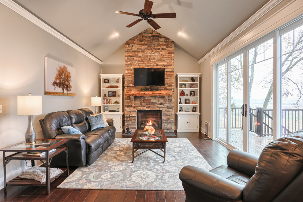 Diseño de sala de estar campestre con paredes grises, suelo de madera en tonos medios, marco de chimenea de piedra y televisor colgado en la pared