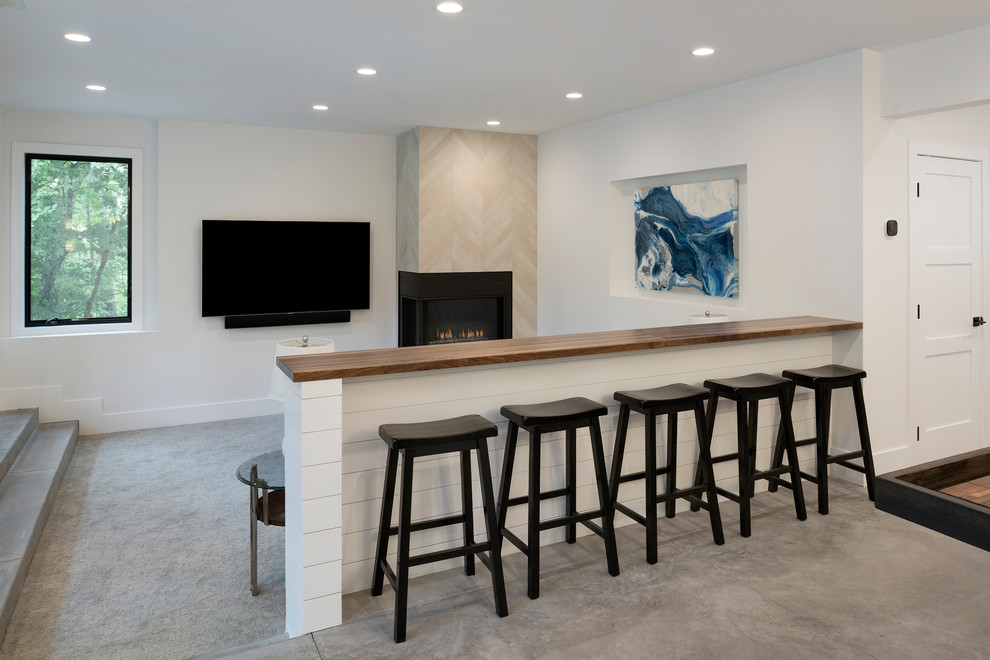 Inredning av ett modernt mellanstort allrum med öppen planlösning, med en hemmabar, vita väggar, betonggolv, en dubbelsidig öppen spis, en spiselkrans i sten, en väggmonterad TV och grått golv