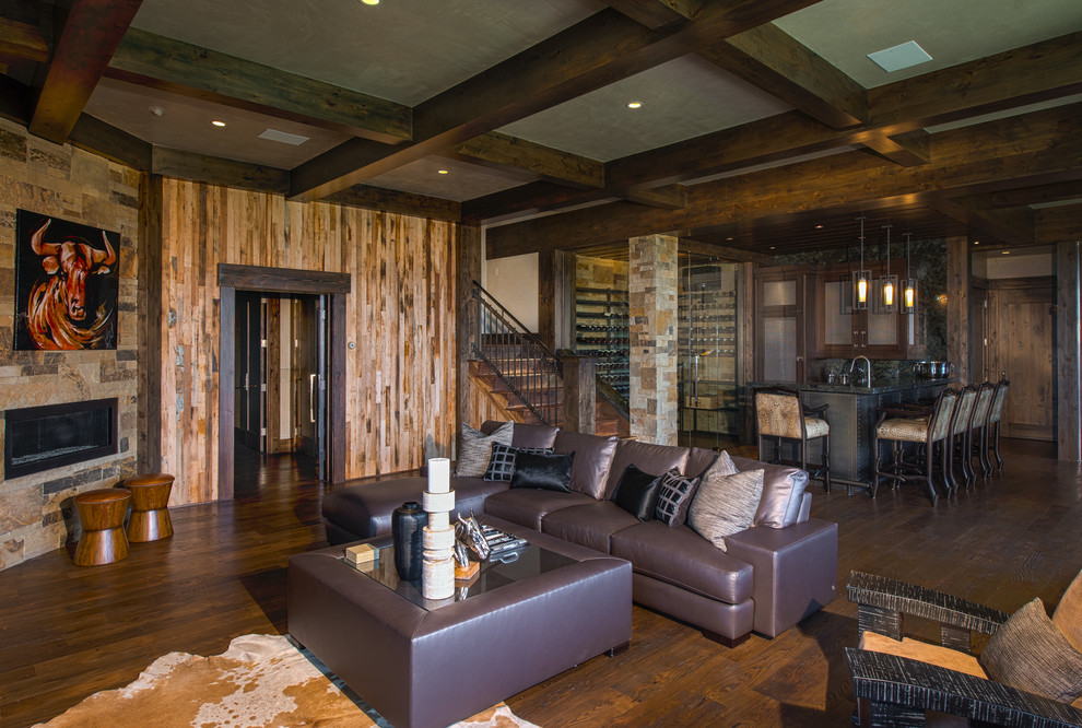Foto de sala de estar con barra de bar abierta rural grande con suelo de madera oscura, chimenea de esquina, marco de chimenea de piedra, televisor colgado en la pared y suelo marrón