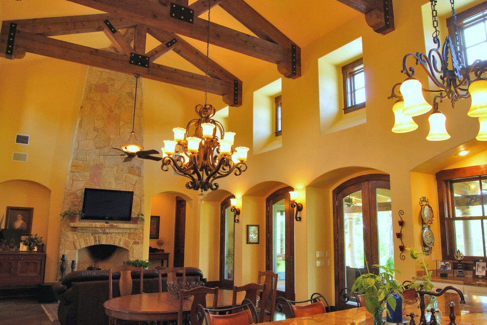 Ejemplo de sala de estar abierta mediterránea grande con paredes beige, suelo de madera oscura, todas las chimeneas, marco de chimenea de piedra y televisor colgado en la pared