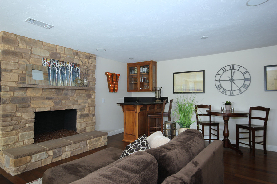 Diseño de sala de estar con barra de bar abierta clásica renovada de tamaño medio con paredes beige, suelo de madera en tonos medios, todas las chimeneas, marco de chimenea de piedra y televisor colgado en la pared