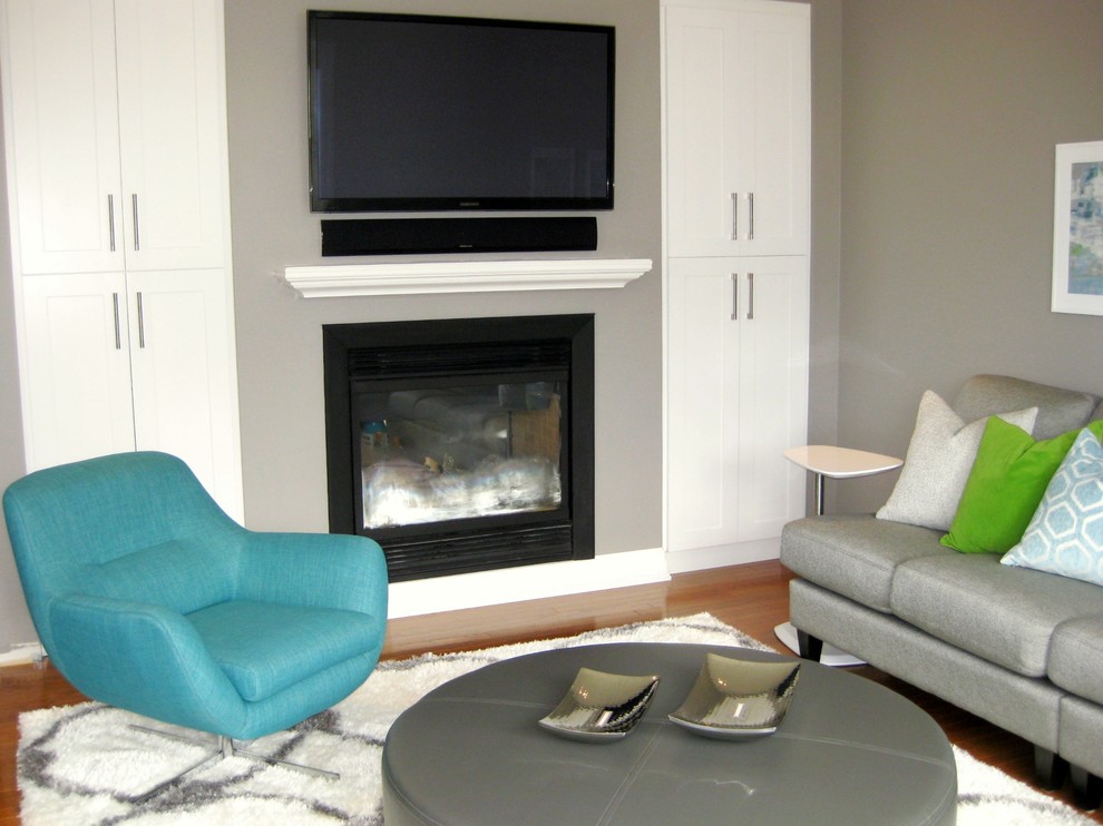 Стильный дизайн: открытая гостиная комната среднего размера в стиле модернизм с серыми стенами, светлым паркетным полом, двусторонним камином, телевизором на стене и фасадом камина из штукатурки - последний тренд