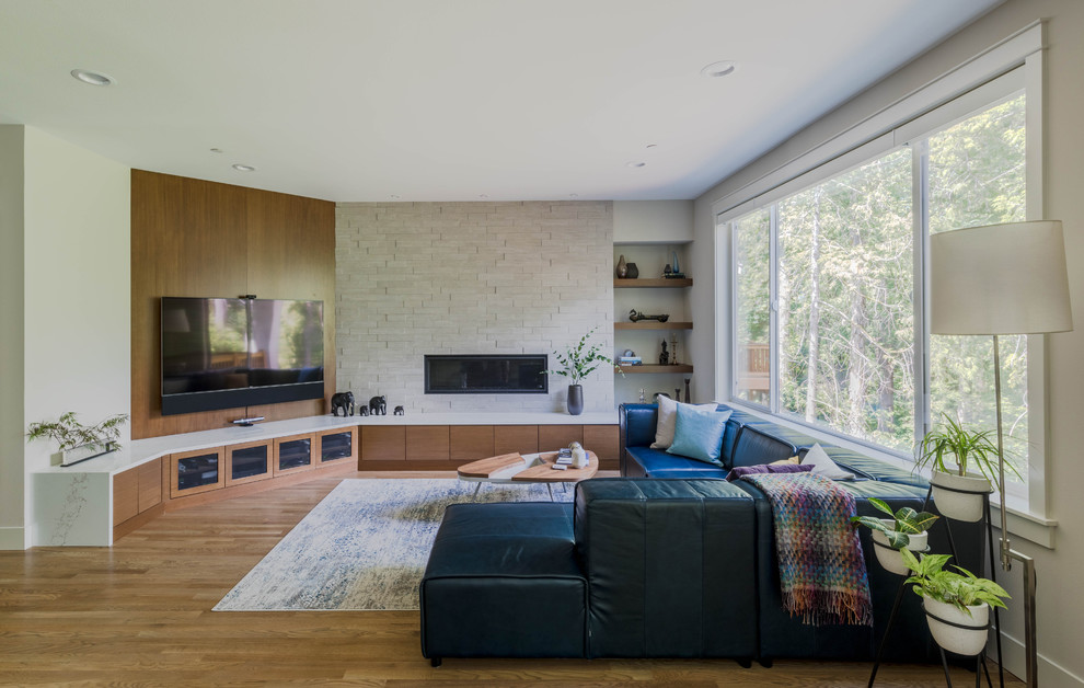 Diseño de sala de estar abierta contemporánea grande con paredes beige, suelo de madera clara, chimenea lineal, marco de chimenea de piedra, televisor colgado en la pared, suelo marrón y alfombra