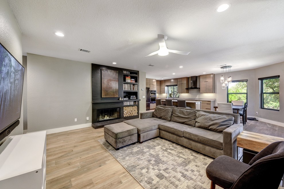 Großes, Abgetrenntes Modernes Wohnzimmer mit grauer Wandfarbe, hellem Holzboden, Kamin, Kaminumrandung aus Beton, TV-Wand und beigem Boden in Austin