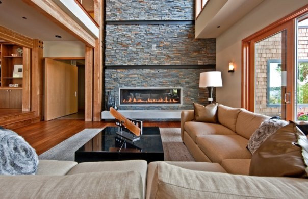 Idée de décoration pour une très grande salle de séjour design ouverte avec un mur beige, un sol en bois brun, une cheminée ribbon et un manteau de cheminée en pierre.