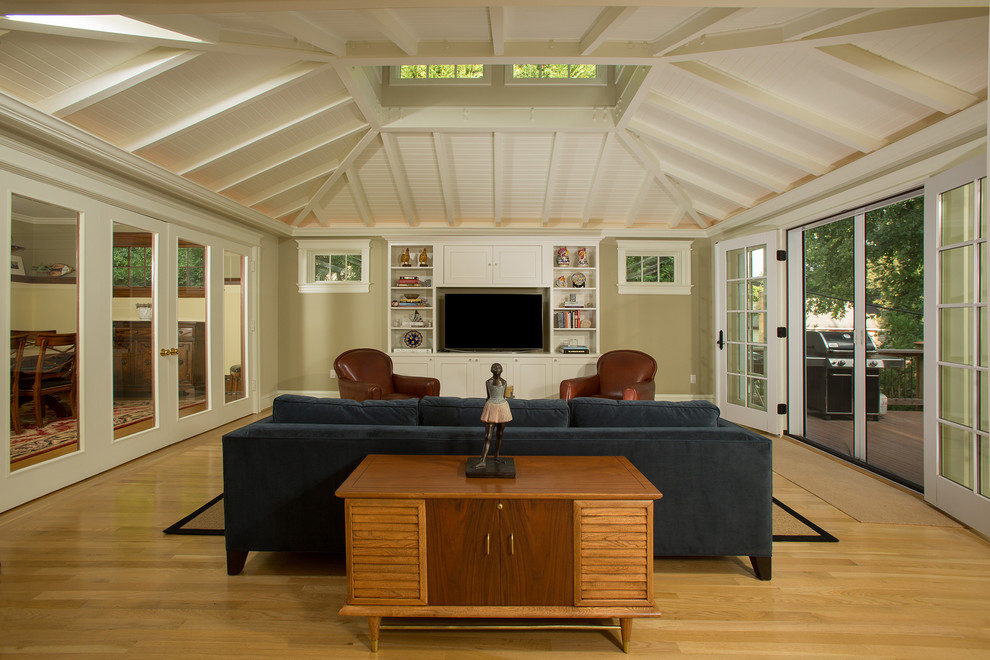 Imagen de sala de estar abierta tradicional renovada grande sin chimenea con paredes beige, suelo de madera clara y pared multimedia