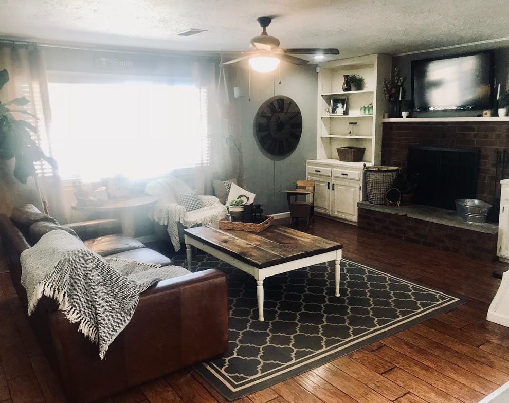 Imagen de sala de estar abierta de estilo de casa de campo de tamaño medio con paredes grises, suelo laminado, todas las chimeneas, marco de chimenea de ladrillo, televisor colgado en la pared y suelo marrón