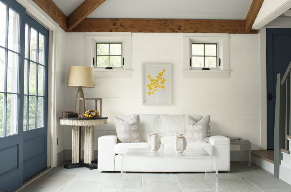 На фото: гостиная комната в стиле кантри с белыми стенами, полом из известняка и серым полом с