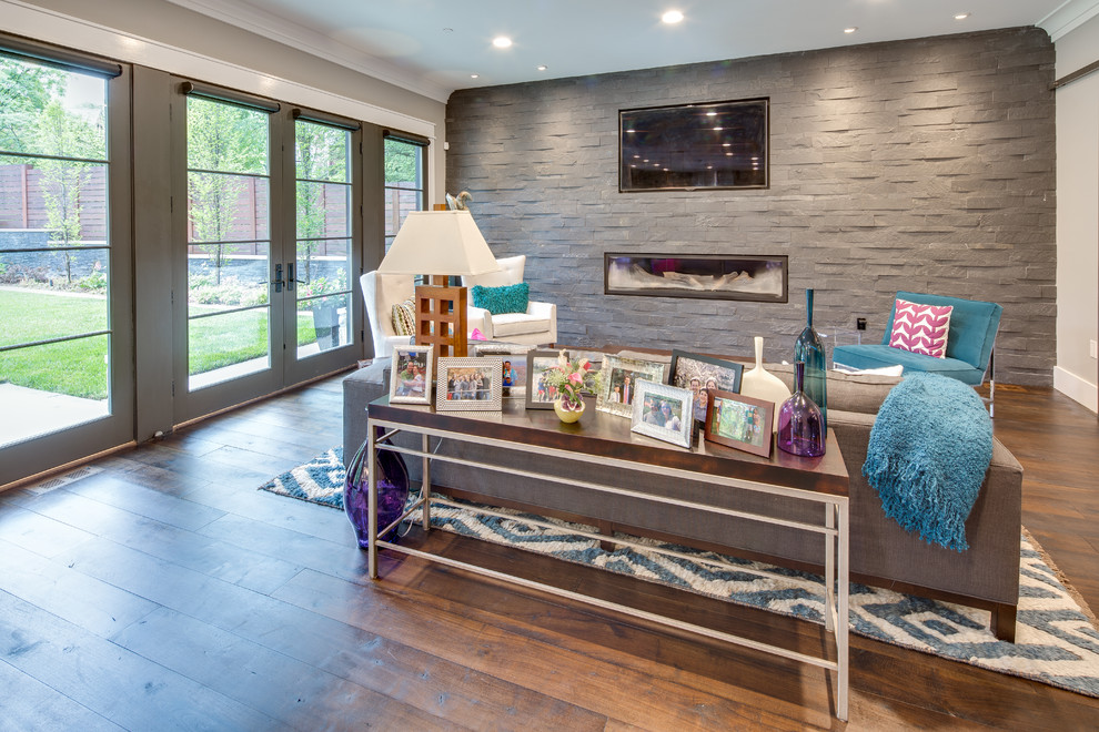 Diseño de sala de estar abierta contemporánea grande con paredes grises, suelo de madera en tonos medios, chimenea lineal, marco de chimenea de piedra y televisor colgado en la pared