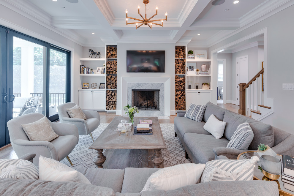 Modelo de sala de estar abierta clásica renovada grande con paredes grises, suelo de madera en tonos medios, todas las chimeneas, marco de chimenea de piedra, televisor colgado en la pared y casetón