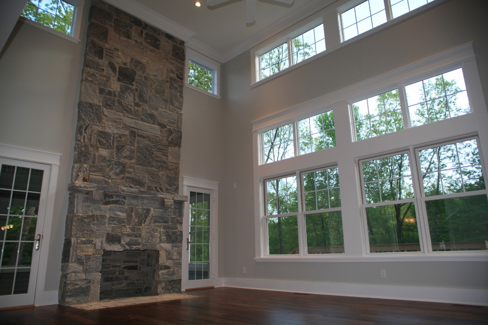 Ejemplo de sala de estar abierta tradicional sin televisor con chimeneas suspendidas, marco de chimenea de piedra, suelo de madera oscura y paredes grises