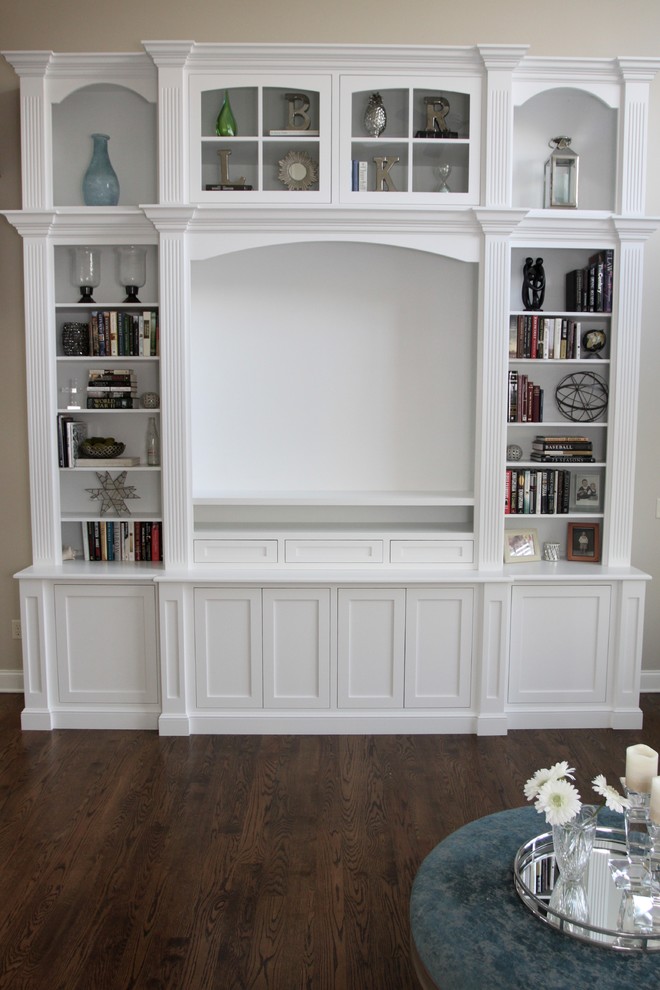 Modelo de sala de estar con biblioteca abierta clásica grande sin chimenea con paredes beige, suelo de madera oscura, pared multimedia y suelo marrón