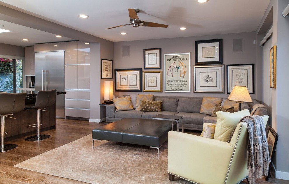Modelo de sala de estar abierta contemporánea de tamaño medio sin chimenea con paredes grises, suelo de madera en tonos medios y televisor colgado en la pared