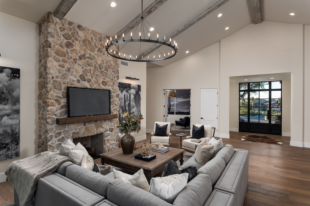 Mediterranes Wohnzimmer mit beiger Wandfarbe, Kamin, Kaminumrandung aus Stein, TV-Wand, braunem Boden und braunem Holzboden in Phoenix