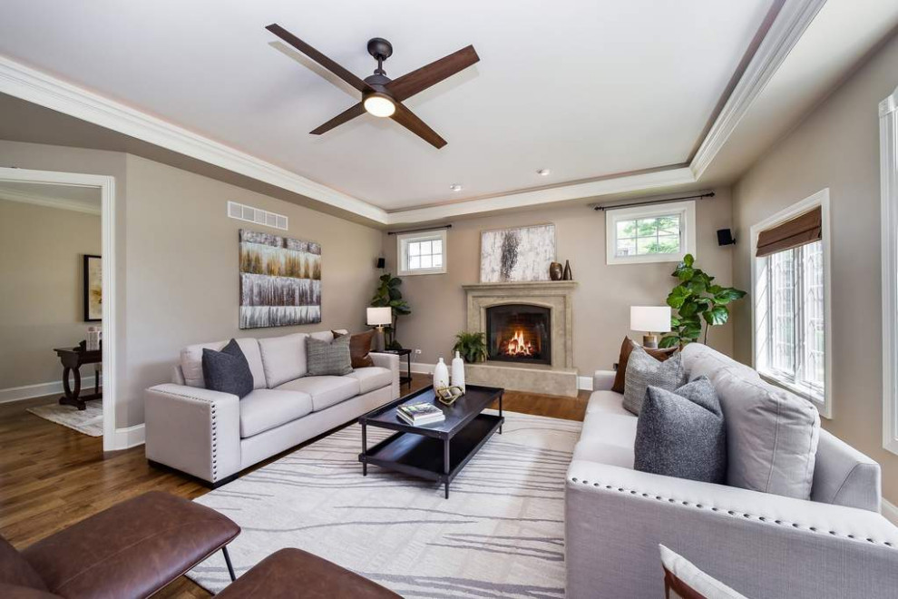 Example of a large transitional enclosed medium tone wood floor, brown floor and tray ceiling family room design in Chicago with gray walls, a standard fireplace and no tv