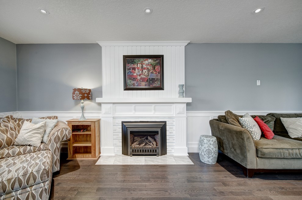 Photo of a medium sized traditional open plan games room in Calgary with grey walls, medium hardwood flooring, a standard fireplace, a tiled fireplace surround, no tv and brown floors.