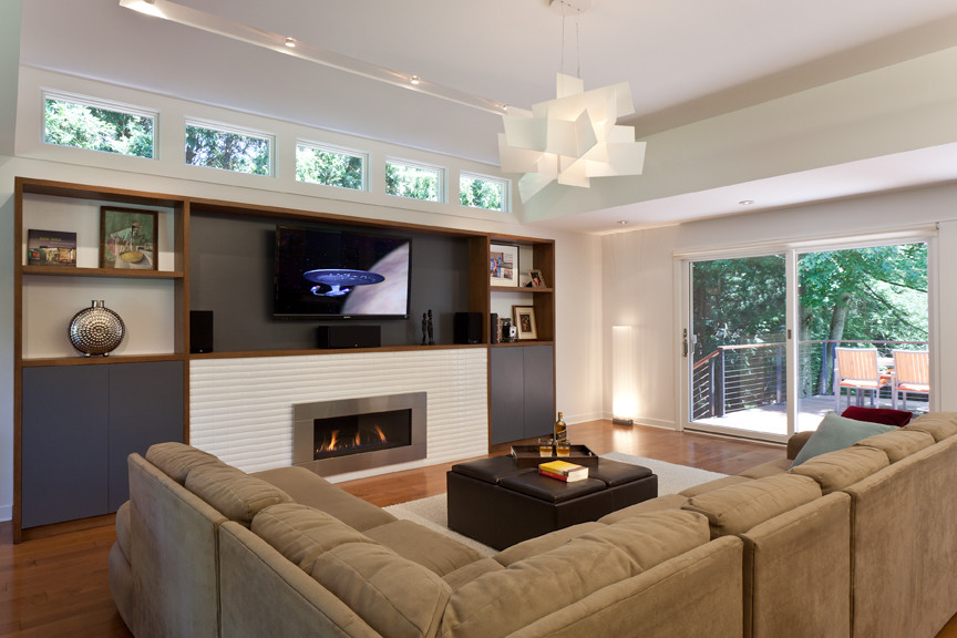 На фото: гостиная комната в стиле модернизм с паркетным полом среднего тона, стандартным камином, фасадом камина из плитки и телевизором на стене