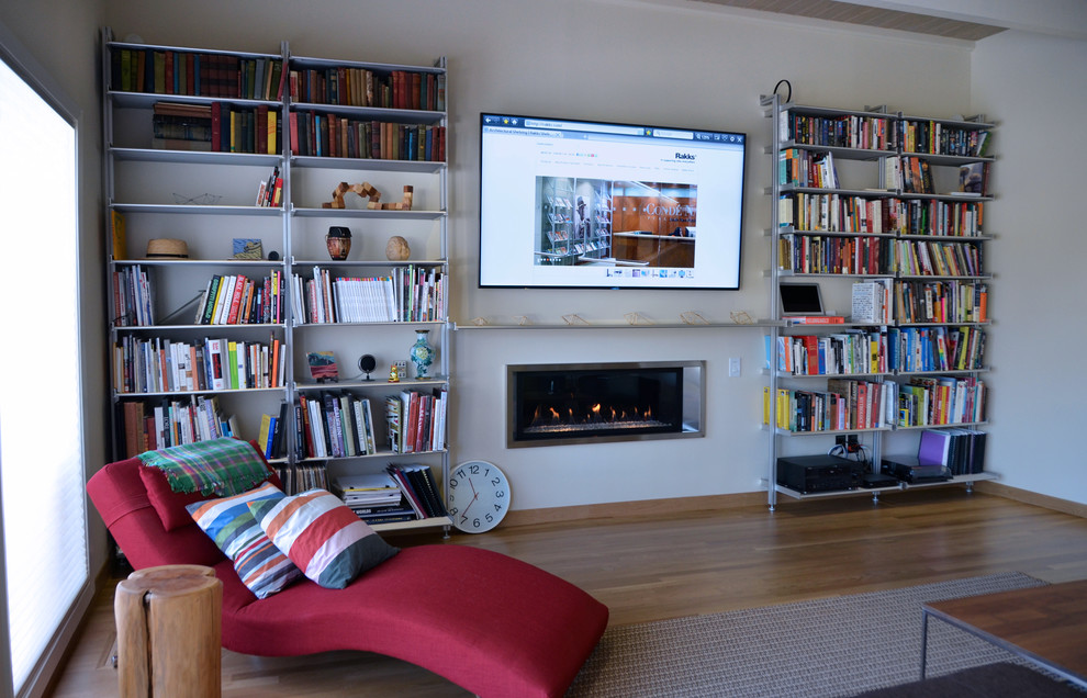 На фото: большая открытая гостиная комната в стиле модернизм с с книжными шкафами и полками и телевизором на стене