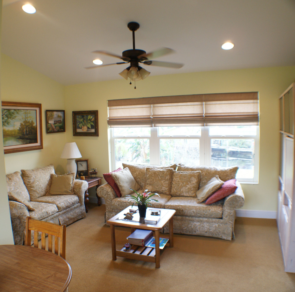 Imagen de sala de estar abierta exótica de tamaño medio sin chimenea y televisor con paredes amarillas, moqueta y suelo beige