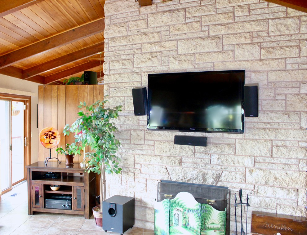 ポートランドにある広いトロピカルスタイルのおしゃれなオープンリビング (ベージュの壁、セラミックタイルの床、標準型暖炉、石材の暖炉まわり、壁掛け型テレビ、茶色い床) の写真