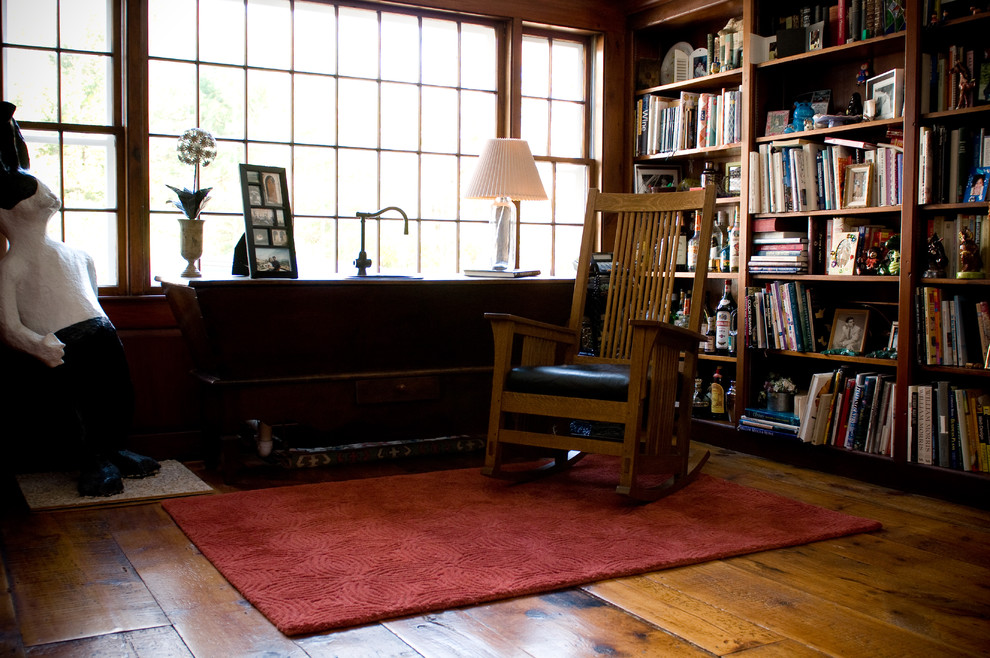 На фото: большая открытая гостиная комната в стиле кантри с с книжными шкафами и полками, коричневыми стенами и темным паркетным полом с