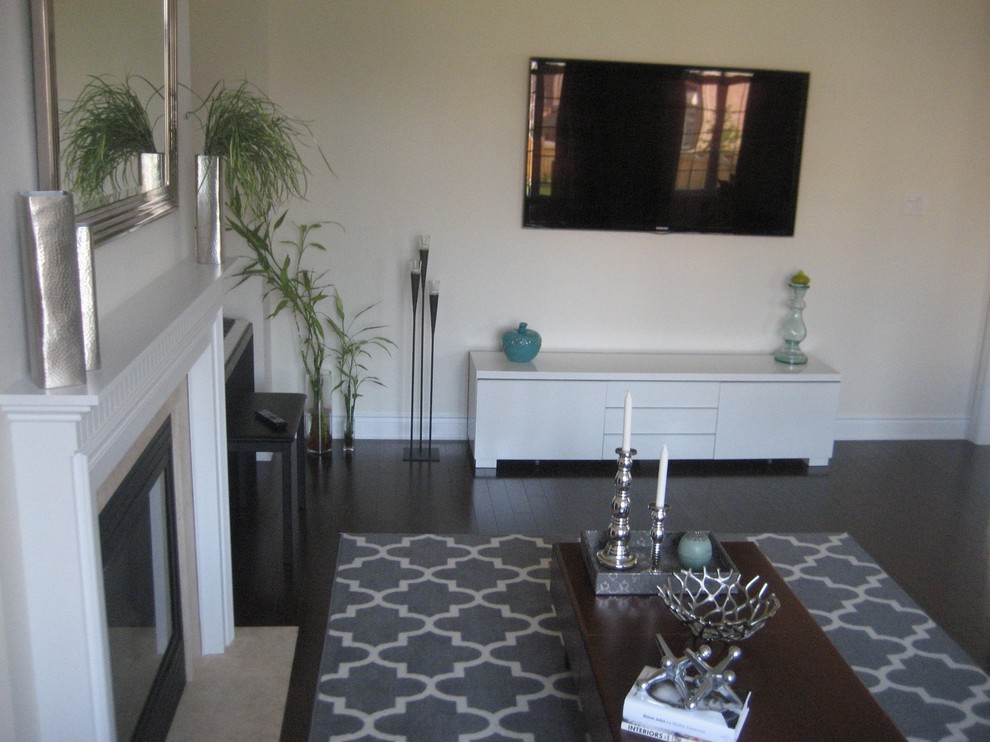 Exemple d'une grande salle de séjour tendance fermée avec un mur beige, un sol en bois brun, une cheminée standard et un téléviseur fixé au mur.