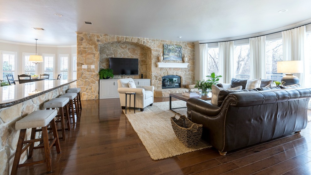 Modelo de sala de estar abierta tradicional renovada grande con paredes grises, suelo de madera en tonos medios, todas las chimeneas, marco de chimenea de piedra y televisor colgado en la pared