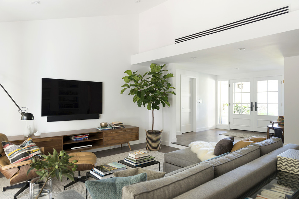 Imagen de sala de estar abierta contemporánea grande sin chimenea con paredes blancas, suelo de madera en tonos medios y televisor colgado en la pared