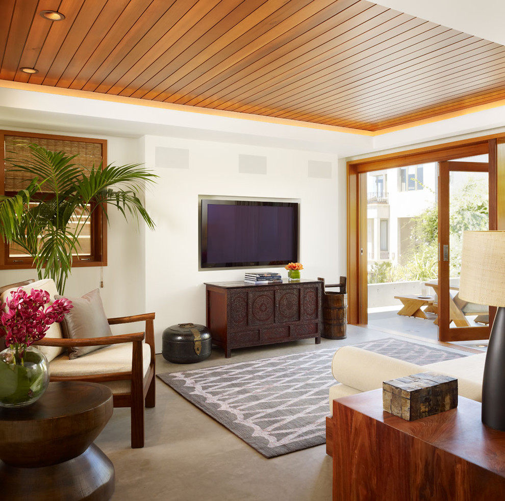 Ejemplo de sala de estar abierta exótica de tamaño medio con paredes blancas, televisor colgado en la pared, suelo de cemento y suelo gris