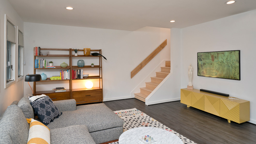 Esempio di un soggiorno minimalista di medie dimensioni e aperto con libreria, pareti bianche, pavimento in laminato, nessun camino, TV a parete e pavimento grigio