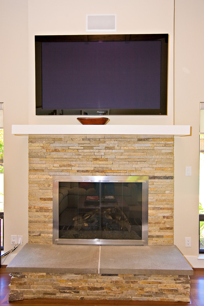 This is an example of a large contemporary open plan games room in San Francisco with white walls, medium hardwood flooring, a standard fireplace, a stone fireplace surround and a wall mounted tv.